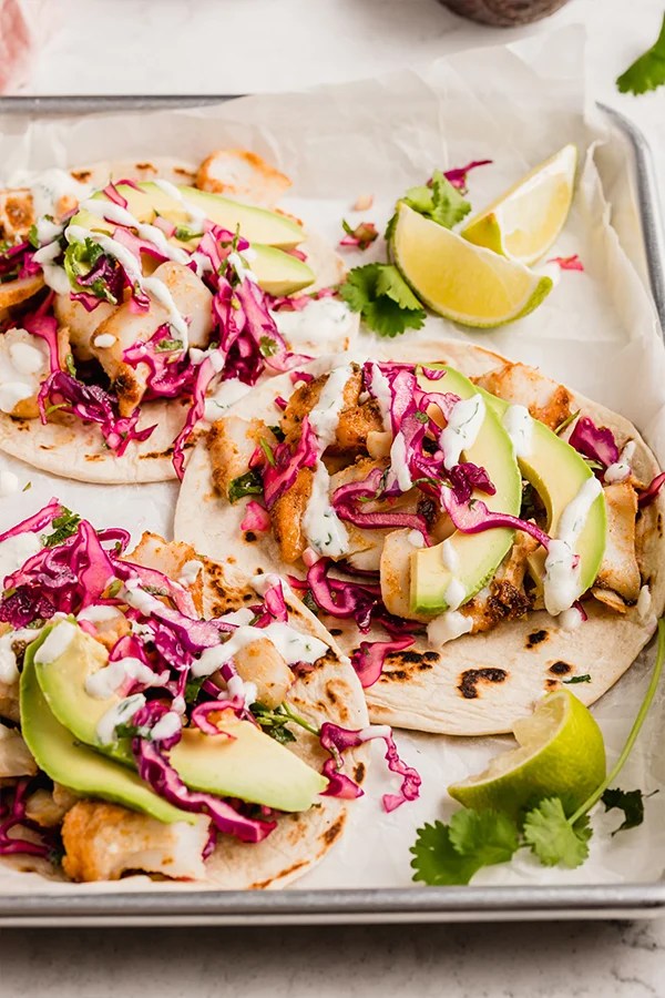 Three fish tacos on a serving tray with lime and cilantro