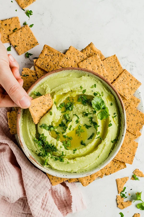Cracker dipping into avocado hummus