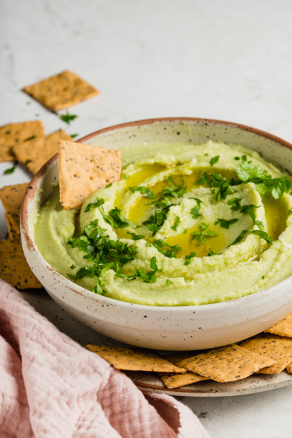 Cracker in a bowl of avocado cauliflower hummus.