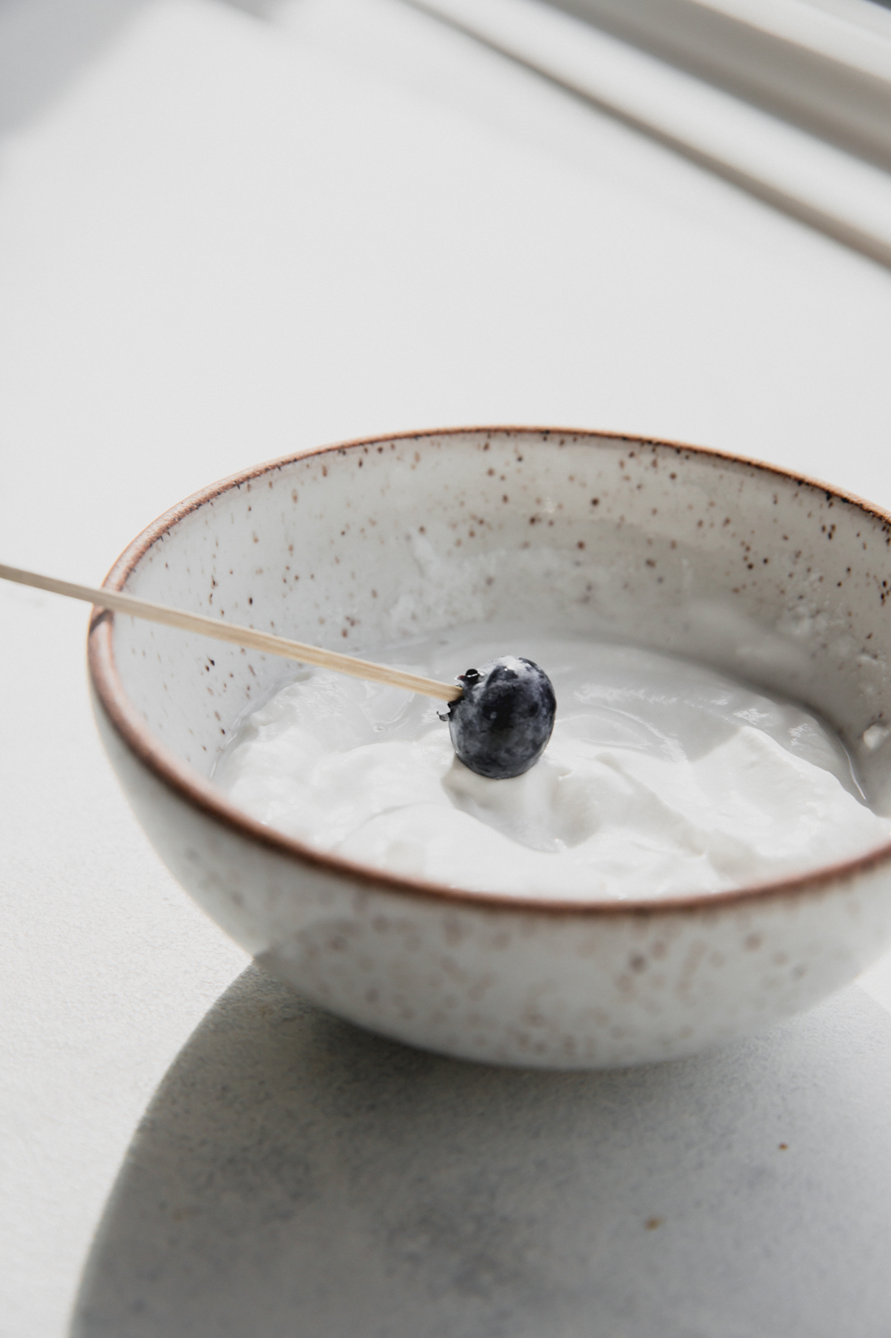 Blueberry on a tooth pick dipping in yogurt.