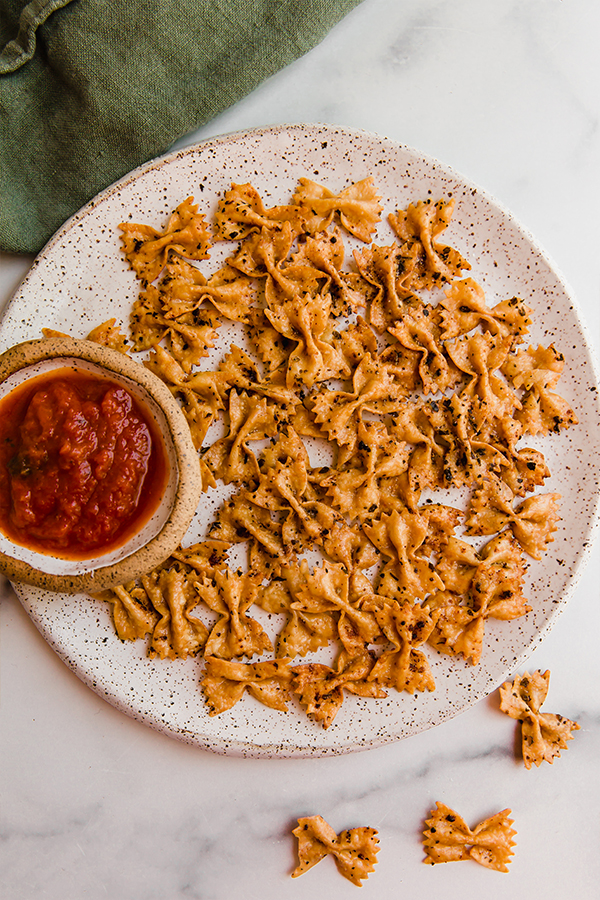 Bowl of dip on a plate of pasta chips.