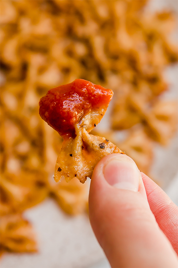 Person holding a pasta chip dipped in sauce.