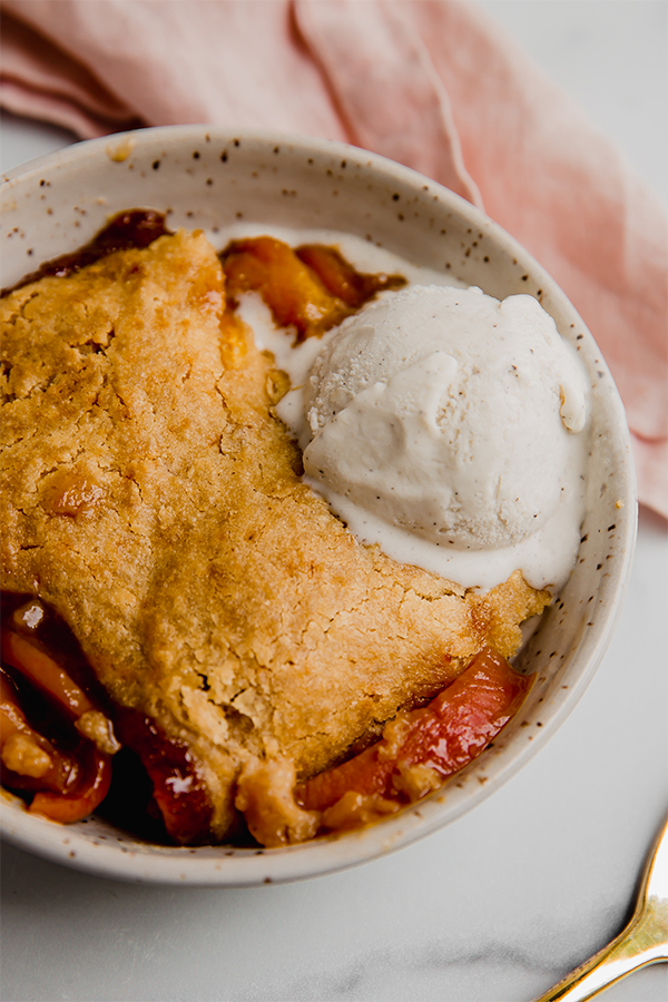 Ice cream over peach cobbler in a bowl.