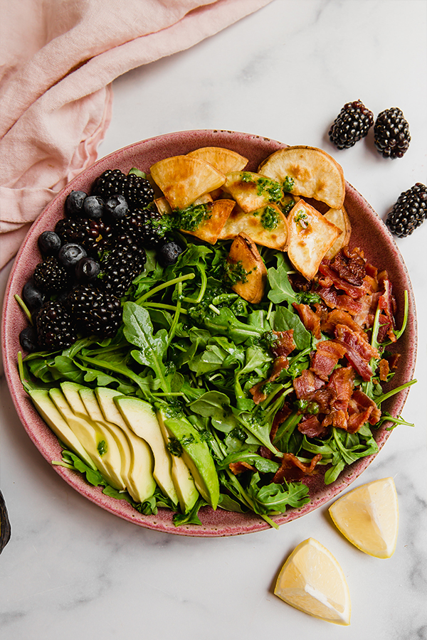 Top view of breakfast salad topped with bacon, avocado, sweet potato, and berries