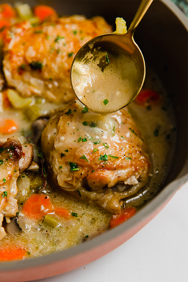 Spoon pouring sauce over chicken in a pan.