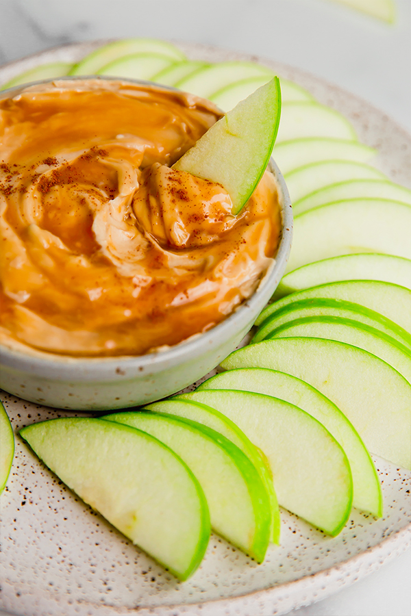 An apple slice dipping into creamy caramel apple dip.