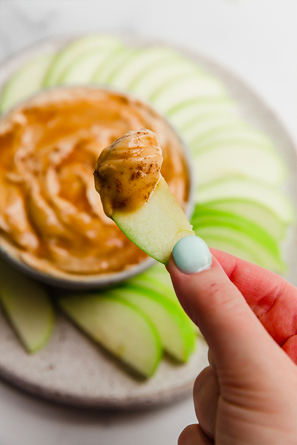 One apple slice with creamy caramel apple dip on it being held by a hand.