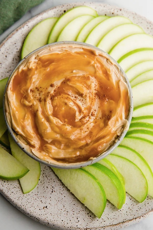Creamy caramel apple dip surrounded by apple slices on a plate.
