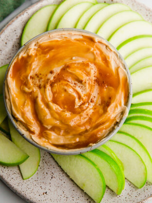Apple slices around a bowl of creamy caramel apple dip.