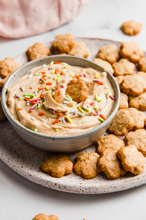Cookie dipped into a bowl with dip and sprinkles.