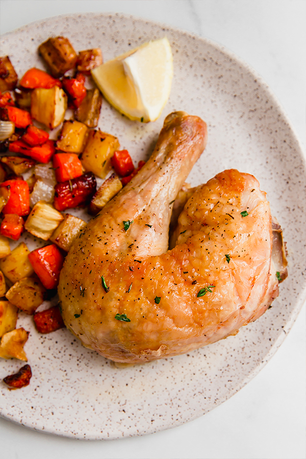 A plate with chicken, roasted vegetables, and a lemon wedge.