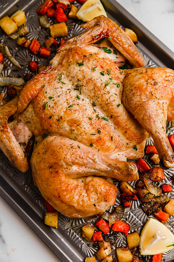 A baking sheet with a cooked chicken and chopped roasted veggies.