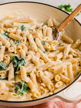 Penne alfredo in a pot with a wooden spoon.