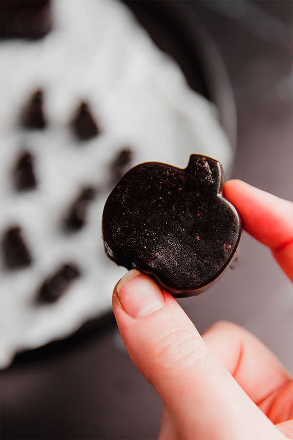 A spooky gummy molded into a pumpkin being held by a few fingers.