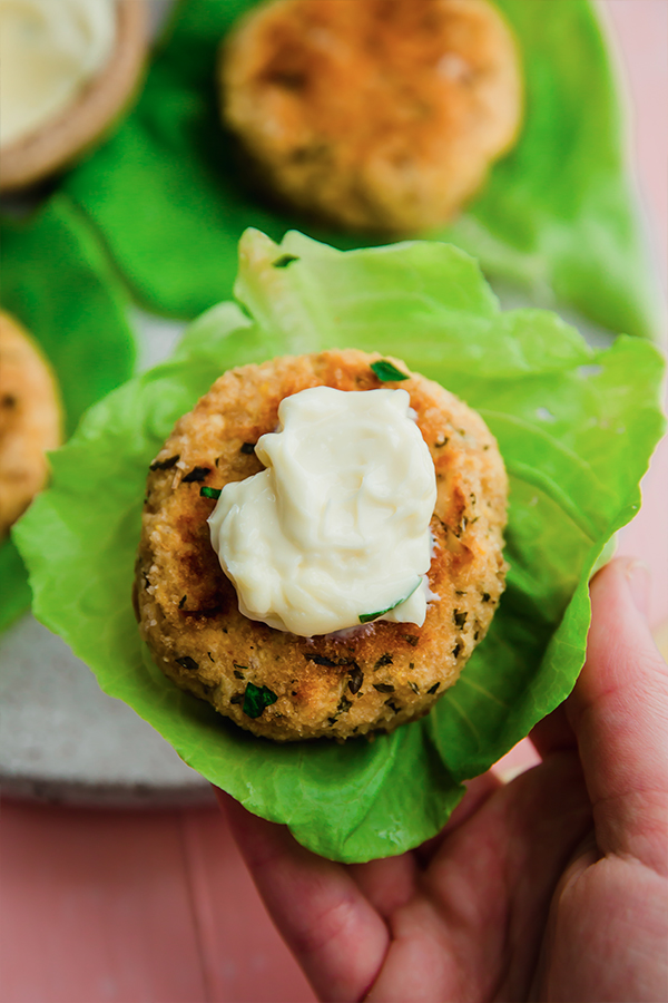 A hand picking up a butternut salmon cake in lettuce.