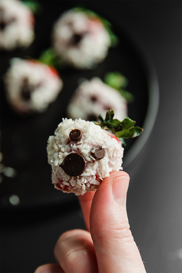 Person holding a strawberry decorated to look like a ghost.
