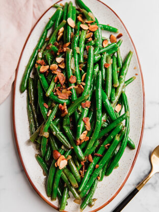 Green beans topped with bacon and toasted almonds on a platter.