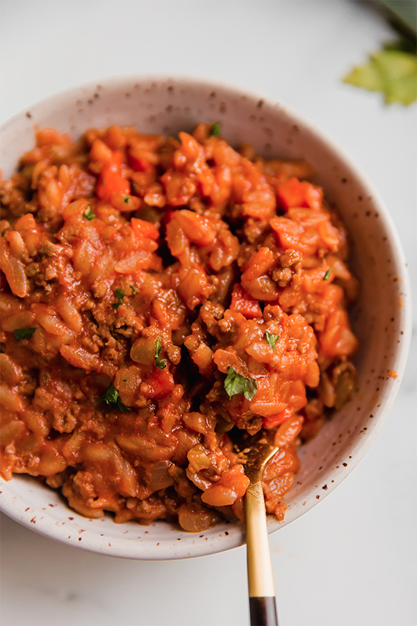 A bowl of orzo bolognese with a fork in it.