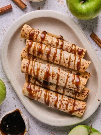 Apple pie roll ups on a platter drizzled with caramel.