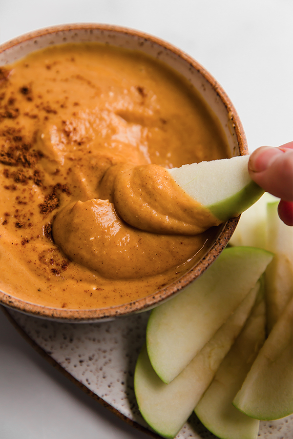 An apple dipping into a bowl of pumpkin pie dip.