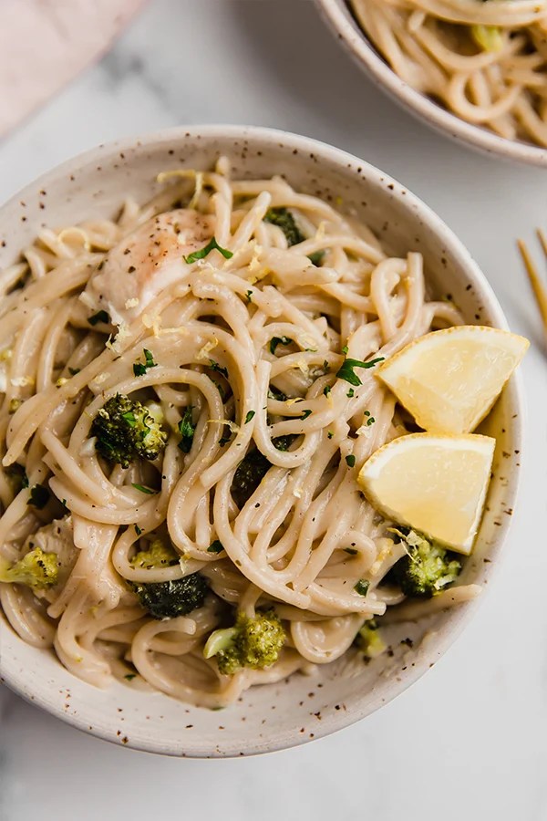 Lemon chicken pasta in a bowl with lemon wedges.