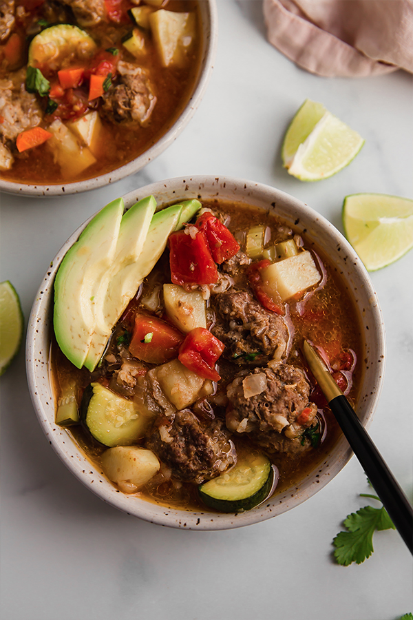 A bowl of Albondigas soup with a spoon in it.
