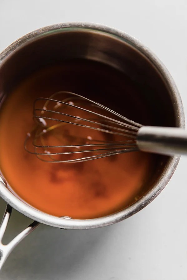 A whisk in a pot dissolving the coconut sugar in the liquid for pickled ginger.