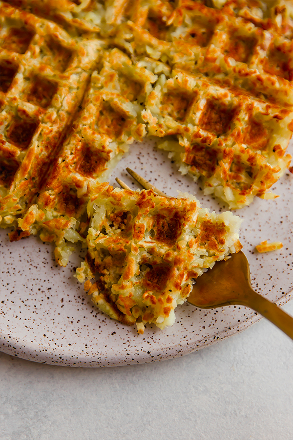 A fork taking a bite out of a hasbrown waffle.