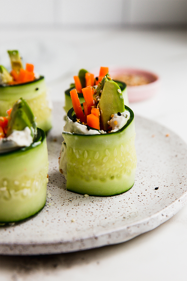 Smoked salmon bagel cucumber rolls standing up on a plate.