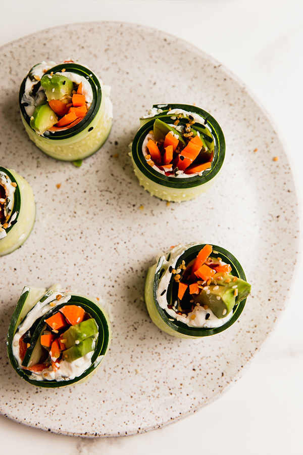 Several smoked salmon bagel cucumber rolls on a plate.