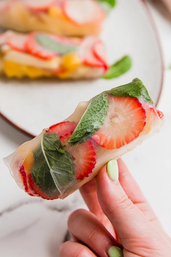 Person holding a fruit spring roll with strawberries.