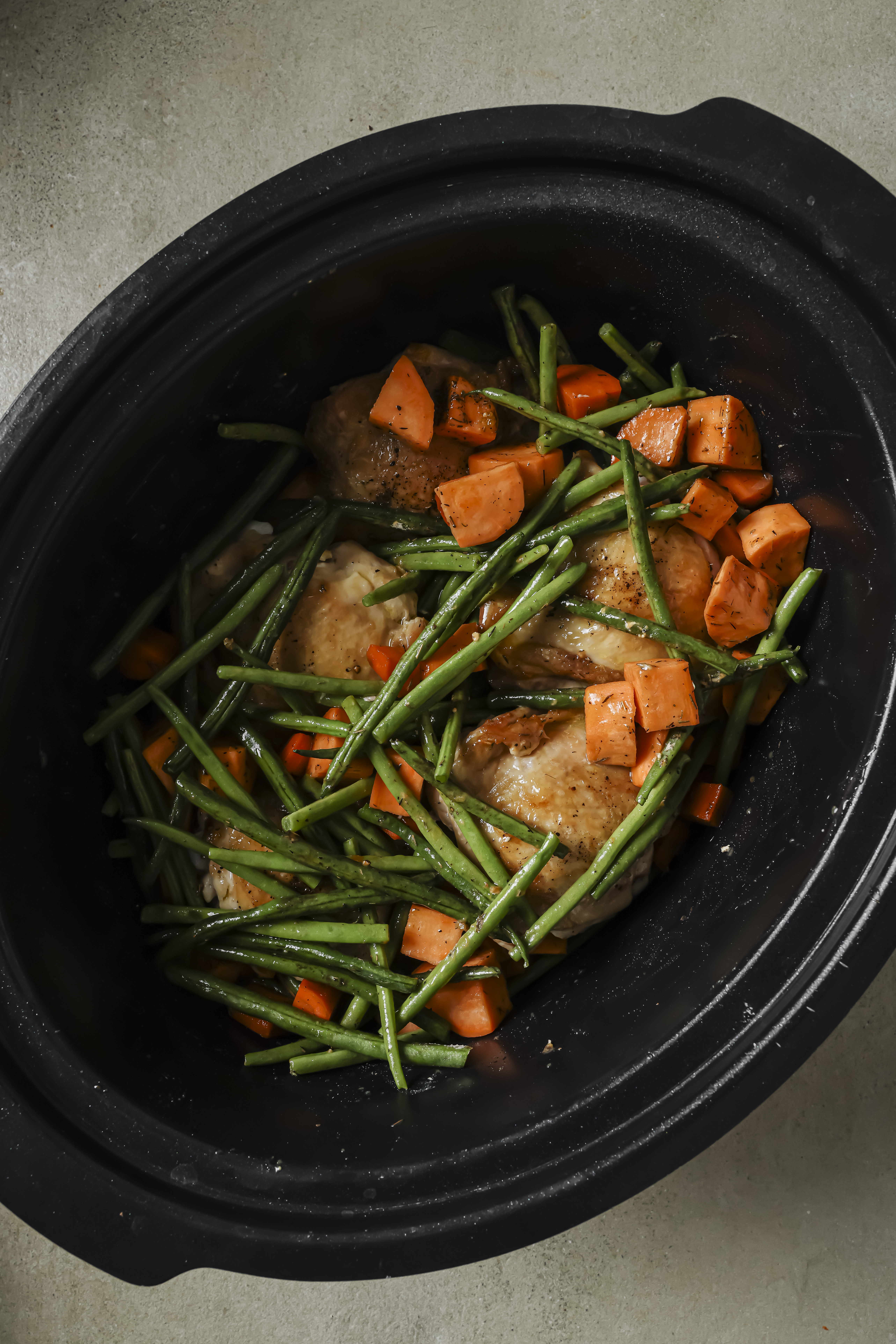 Vegetables over chicken in a slow cooker.