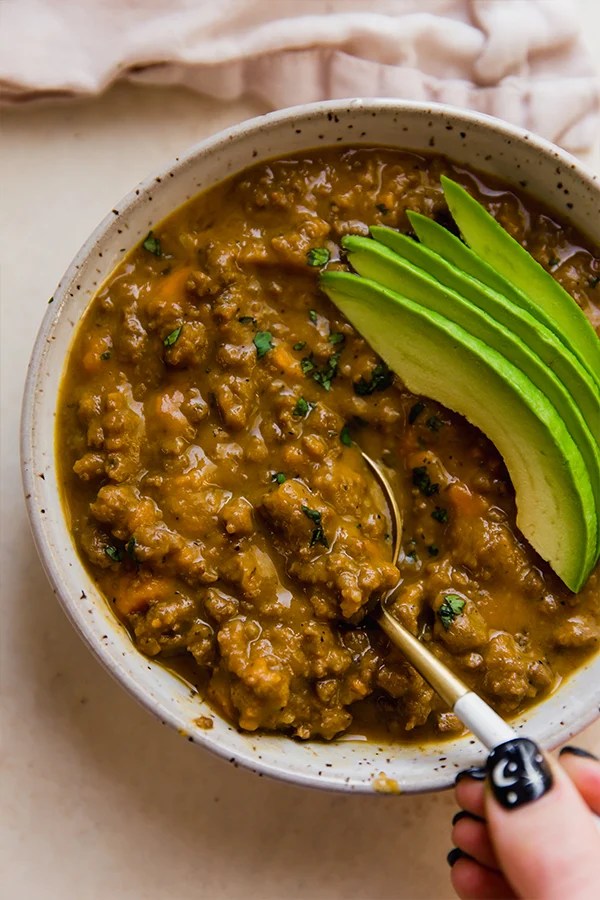 Spoon in a bowl of dairy-free queso chili topped with avocado.