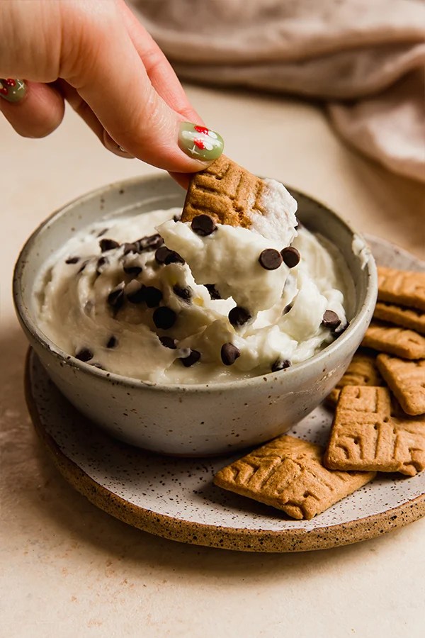 Person dipping a cookie into a bowl of cannoli dip.
