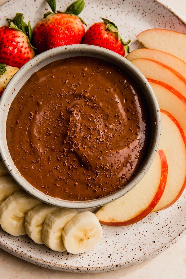 Fruit around a bowl of chocolate dip.