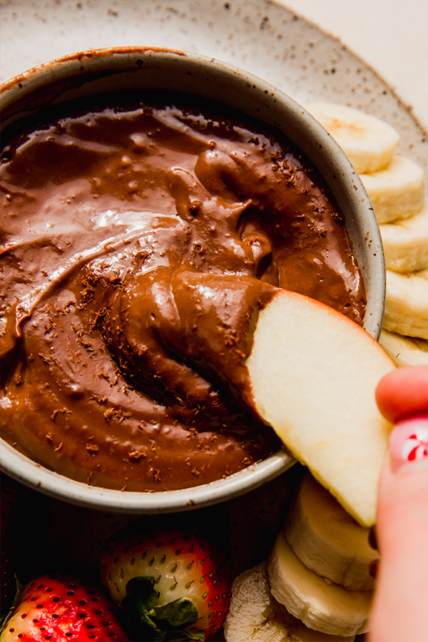 An apple dipping into chocolate fruit dip.