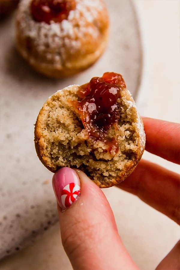 Person holding a jelly donut hole with a bite missing.