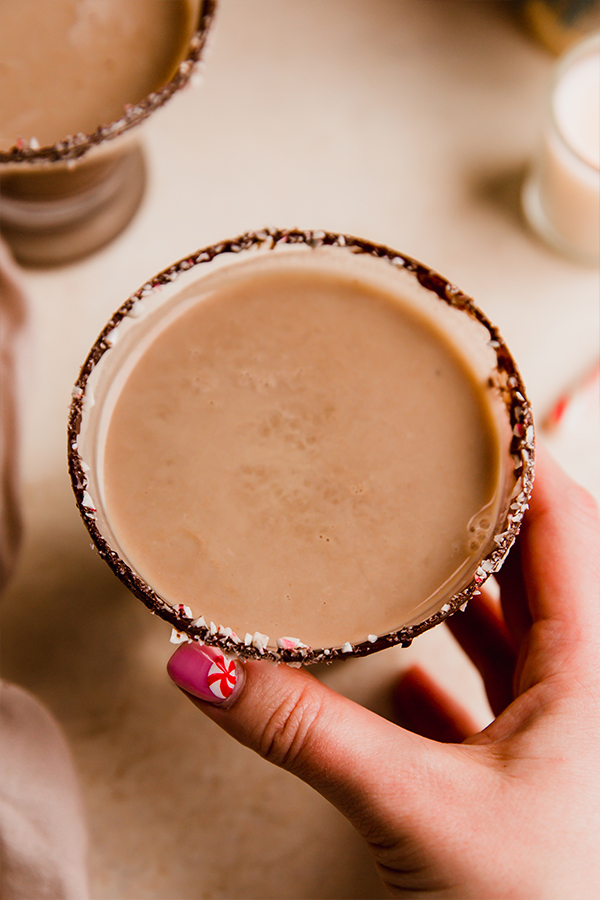 Person grabbing a glass of peppermint mocktail with a chocolate rim.