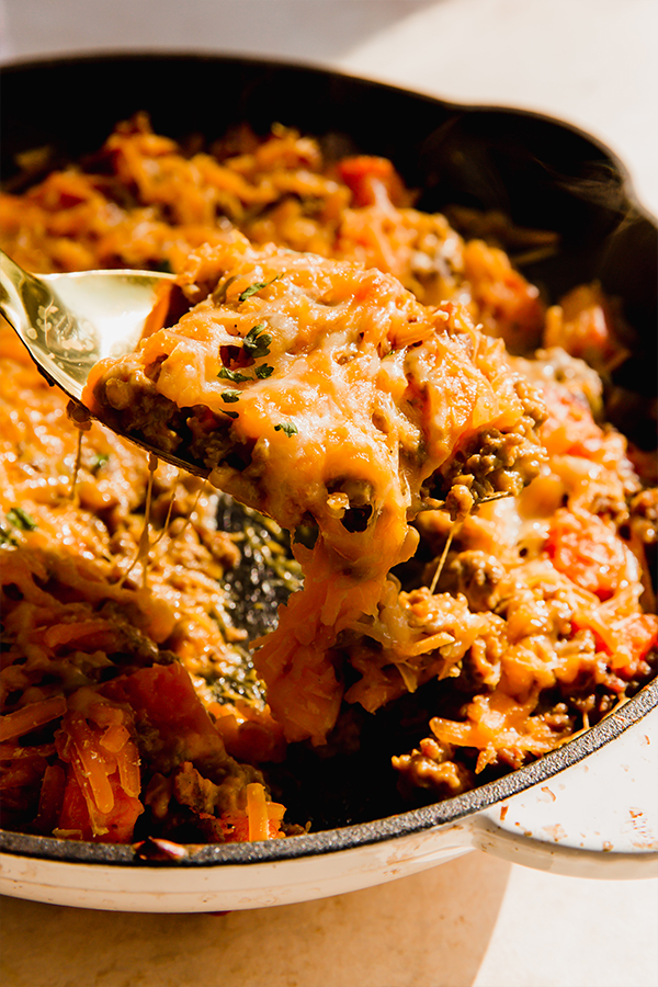 Scoop scooping dairy-free \"cheesy\" beef and sweet potato skillet from a pan.