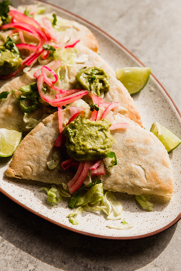 A platter of baked shredded beef tacos topped with onions and guacamole.