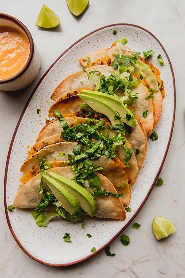 Baked ground beef tacos on a platter topped with avocado.