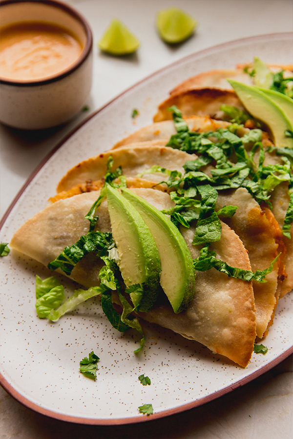 A close-up of baked ground beef tacos topped with avocados and romaine.