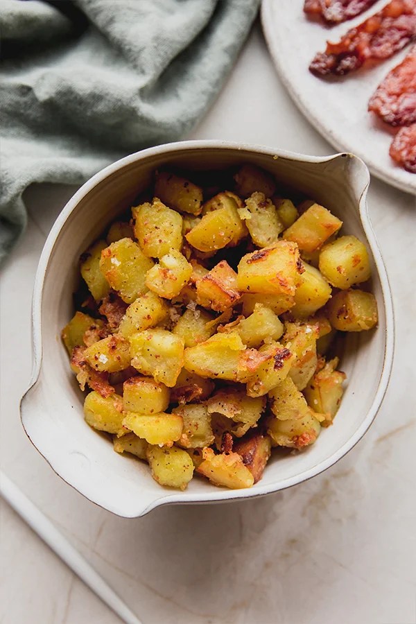 White sweet potatoes in a bowl next to cooked bacon.