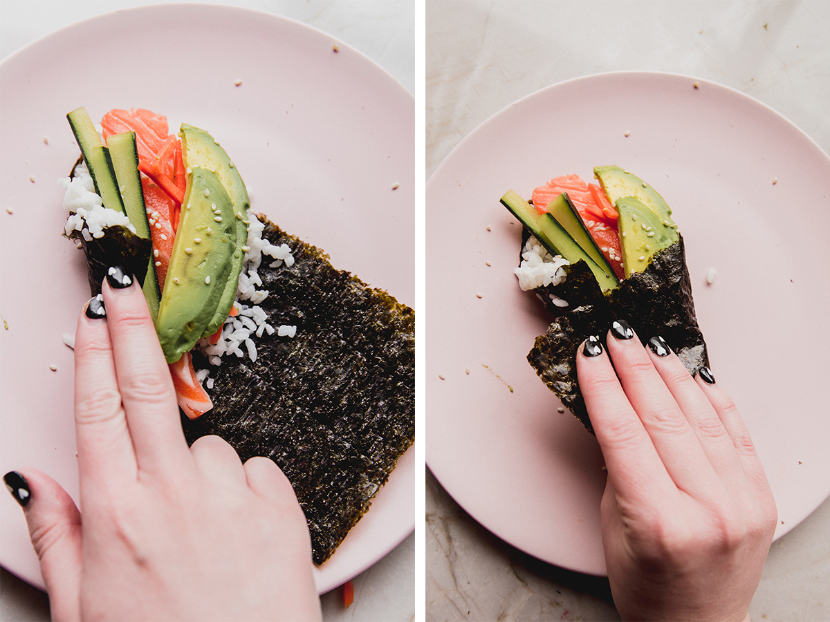 Person rolling a nori sheet over vegetables, rice, and fish.