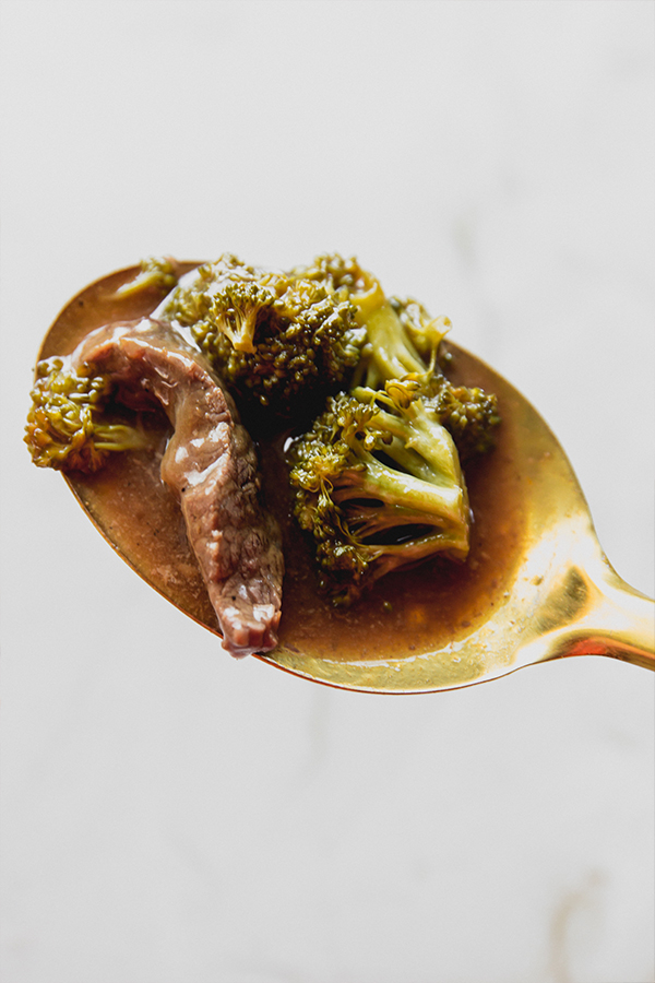 Spoon with a scoop of orange beef and broccoli.