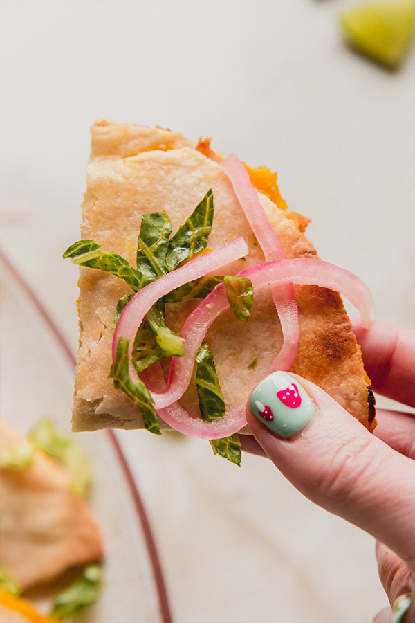 A piece of baked quesadillas with pickled onions in a hand.