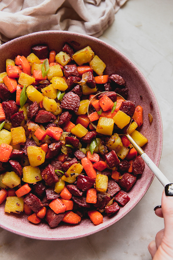 A bowl of healthier hot dog and veggie hash with a serving spoon.