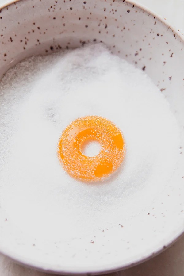 A peach ring gummy being tossed in the sweetner.