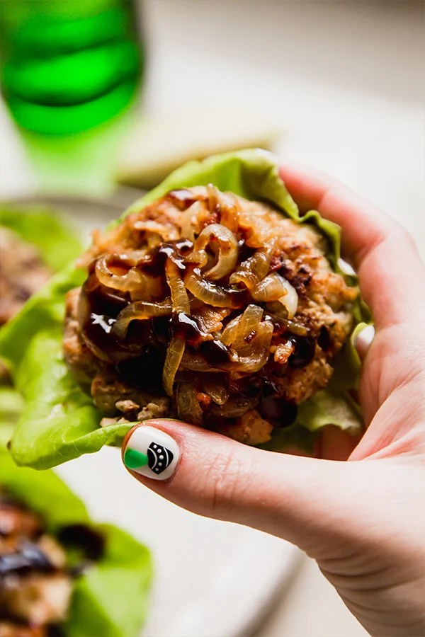 Person holding an apple chicken burger on lettuce.