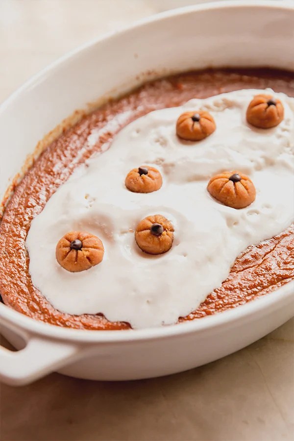 Pumpkin pudding in a baking dish topped with whipped cream and mini pumpkin buckeyes.
